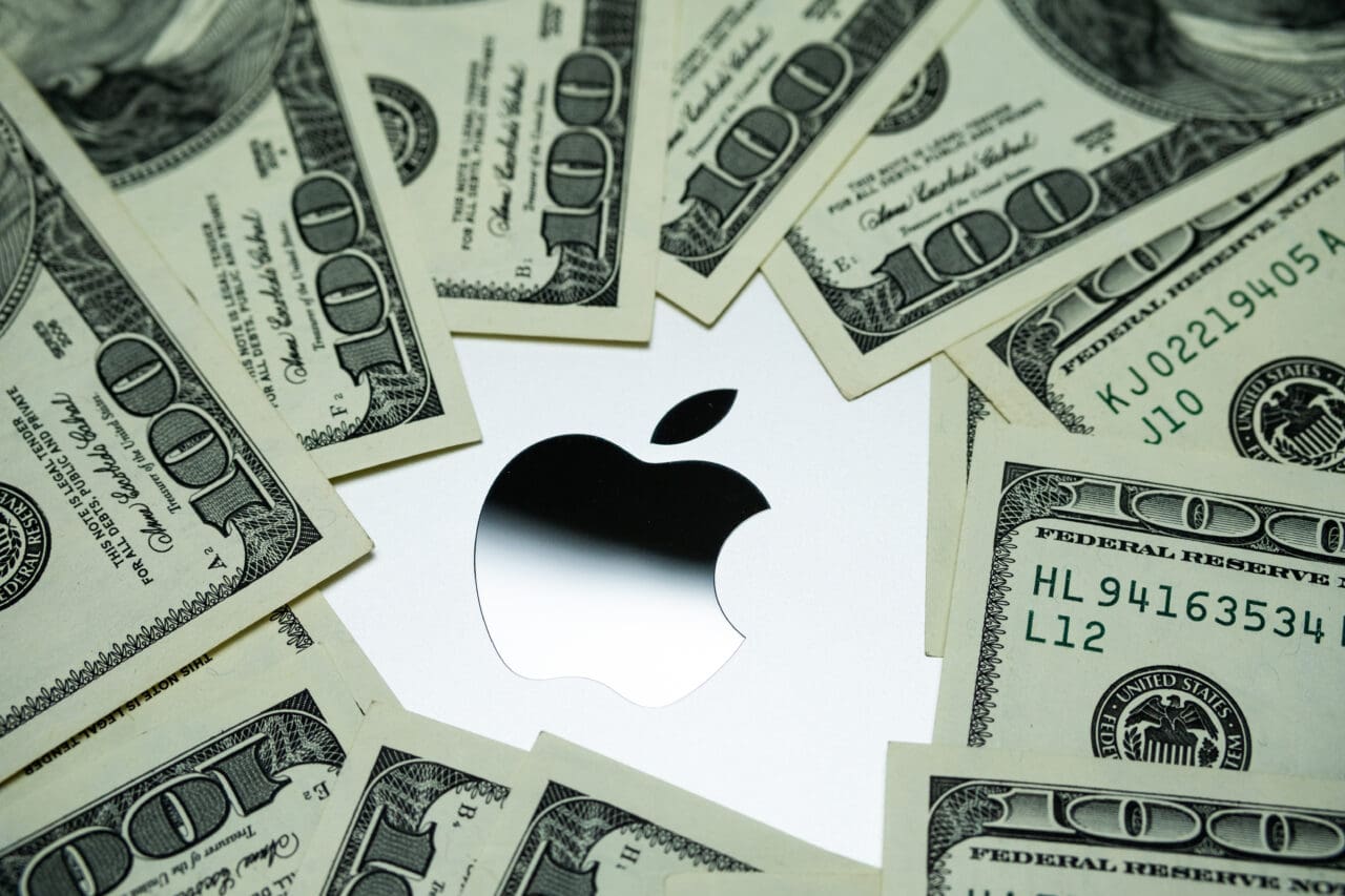 Apple company logo seen on Macbook M1 laptop surrounded by US dollar banknotes. Concept. Selective focus.